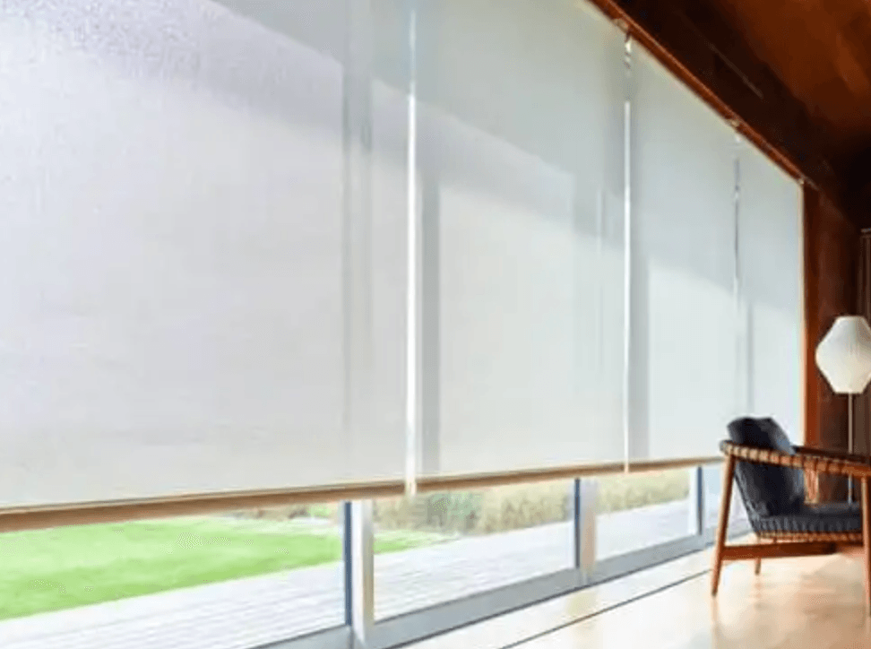 Sheer white roller shades on large windows overlooking a lawn.